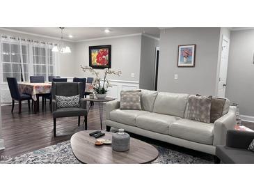 Inviting living room with a white leather sofa, chair, and wooden table, adjacent to dining area with large window at 1436 Sedwick Rd, Durham, NC 27713