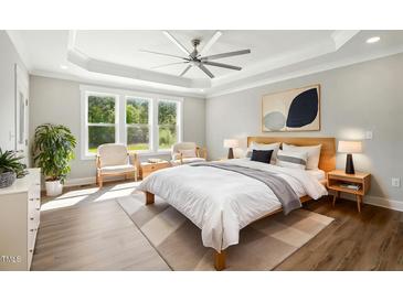 Bright bedroom featuring a ceiling fan, tray ceiling, and large windows providing lots of natural light at 8629 Dukes Lake Rd, Zebulon, NC 27597