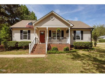 Charming single-Gathering home with a cozy front porch, an American flag, and manicured landscaping at 14 Shire Ct, Zebulon, NC 27597