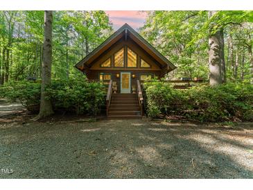 Charming cabin with gable windows, wood siding, surrounded by lush greenery, and a gravel driveway at 300 Rabbit Run, Pittsboro, NC 27312