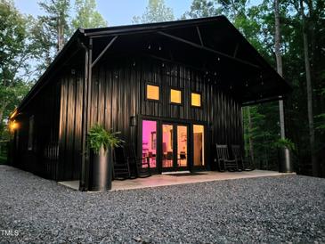 Stunning exterior of a modern black home featuring a gravel driveway and inviting porch with rocking chairs at 665 Lonach Ln, Roxboro, NC 27574