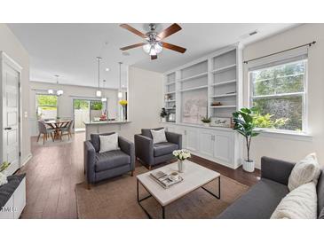 Bright living room featuring hardwood floors, a ceiling fan, large windows, and custom built-in shelves at 7851 Allscott Way, Raleigh, NC 27612