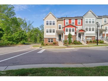 A vibrant townhome with a mix of beige, red, and gray exterior, complemented by lush green trees and grass at 805 Winter Meadow Dr, Wake Forest, NC 27587