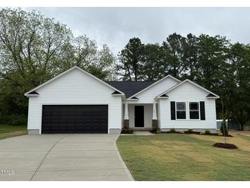 Charming one-story white home with a black garage door and landscaped front yard at 163 Oakfield Trace Dr, Four Oaks, NC 27524