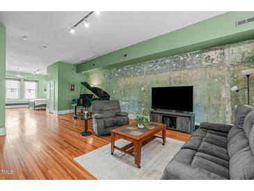 Spacious living room featuring a piano, hardwood floors, and unique accent wall at 323 W Main St # C, Durham, NC 27701