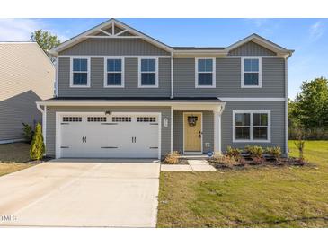 Two-story home with a two-car garage, vinyl siding, tidy landscaping, and a welcoming yellow front door at 473 Lavatera Dr, Wendell, NC 27591