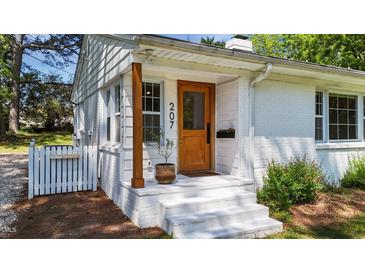 Charming front entrance featuring a wooden door, white brick steps, and beautiful landscaping at 207 N Aiken St, Fuquay Varina, NC 27526