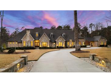 Stunning stone home showcasing manicured lawn, circular drive, and exquisite architectural detail at dusk at 103 Patriot Way, Apex, NC 27523