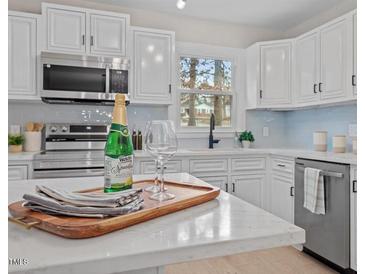 Modern kitchen featuring white cabinets, stainless steel appliances and light backsplash at 3408 Brentwood Rd, Raleigh, NC 27604