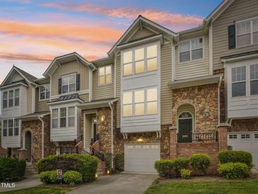 Charming multi-level townhouse featuring stone accents, a garage, and lush landscaping against a vibrant sunset sky at 5026 Celtic Ct, Raleigh, NC 27612