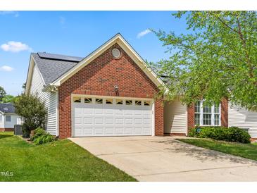 Charming brick home featuring an attached garage, well-manicured lawn, and solar panels on the roof at 210 Millet Dr, Morrisville, NC 27560