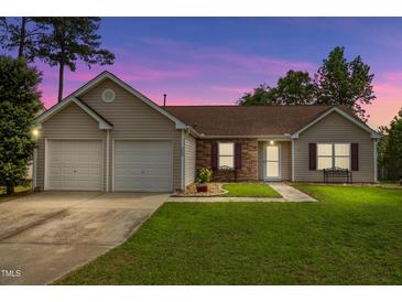 Charming single-story home featuring a well-manicured lawn, two-car garage, and lovely facade at twilight at 308 Holly Briar Dr, Fuquay Varina, NC 27526
