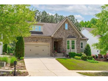 Charming stone home features a manicured lawn, two-car garage, and covered front porch at 525 Morning Oaks Dr, Holly Springs, NC 27540