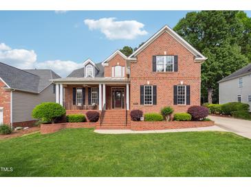 Charming brick home featuring manicured landscaping, a covered front porch, and a classic architectural design at 12428 Penrose Trl, Raleigh, NC 27614
