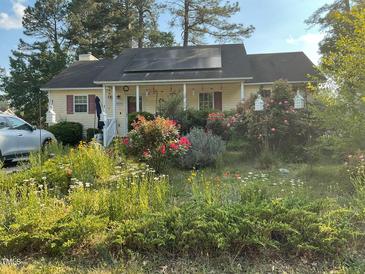 Charming home featuring solar panels, a cozy porch, and beautiful flowerbeds filled with colorful flowers and plants at 5404 Drum Inlet Pl, Raleigh, NC 27610