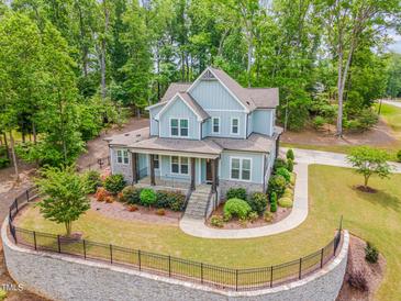 Stunning light blue home with a manicured lawn and stone retaining wall encircled by lush green trees at 251 Gentry Dr, Pittsboro, NC 27312