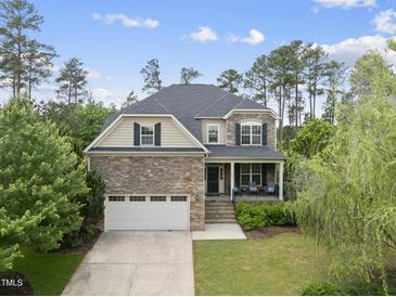 Charming two-story home featuring a stone facade, front porch, attached garage, and landscaped front yard at 449 Sandy Whispers Pl, Cary, NC 27519
