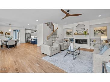 Bright living room featuring hardwood floors, fireplace, staircase, and open access to the kitchen and dining area at 805 Tower St # 102, Raleigh, NC 27607