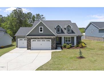 Beautiful exterior featuring stone accents, a three-car garage, and a well-manicured lawn at 86 Buckhaven Ct, Holly Springs, NC 27540
