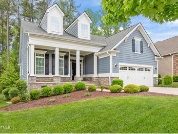Charming blue home featuring a manicured lawn, stone accents, and a welcoming covered front porch at 1620 Hasentree Villa Ln, Wake Forest, NC 27587