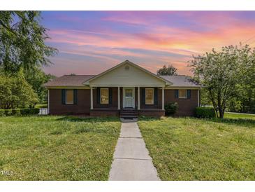 Charming brick home with a manicured lawn and inviting front porch under a beautiful sunset sky at 1303 Cherry Dr, Burlington, NC 27215