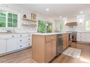 Bright kitchen with stainless steel appliances, light wood cabinets, an island and open shelving at 3009 Hillmer Dr, Raleigh, NC 27609