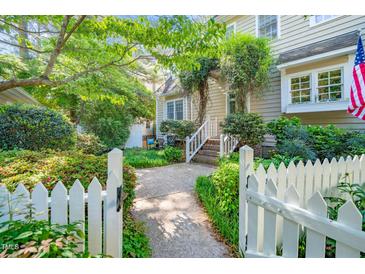 Charming home exterior featuring a welcoming entrance with lush greenery and a white picket fence at 1712 Briarforest Pl, Raleigh, NC 27615