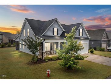Charming two-story home featuring stone accents, a covered porch, and a manicured lawn at sunset at 47 Scarlet Bell Dr, Youngsville, NC 27596