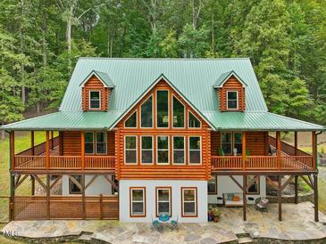 Stunning log home with green metal roof, large windows and wraparound porch surrounded by lush greenery at 123 Beech Forest Way, Pittsboro, NC 27312