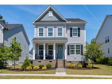 Charming two-story home featuring a welcoming porch with a blue front door and beautiful landscaping at 3224 Wishing Well Wynd, Apex, NC 27502