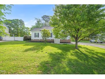 Well-manicured lawn and mature trees accent this charming single-story home with neutral siding and dark shutters at 6324 Daybreak Dr, Wake Forest, NC 27587