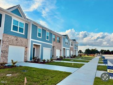 View of new townhomes featuring brick and siding exteriors, white garages, landscaping, and sidewalks under a bright, cloudy sky at 117 N Chubb Rdg, Wilson's Mills, NC 27520