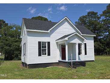 Charming white home with black shutters, front porch, and a well-manicured lawn and mature trees in the background at 305 E Harnett St, Benson, NC 27504