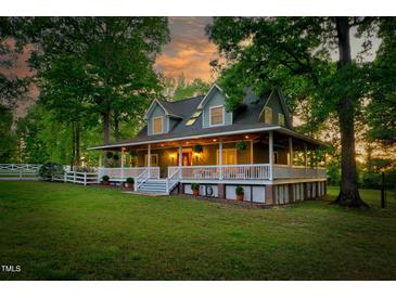 Charming home with a wraparound porch, white railings, lush lawn and mature trees create a serene setting at 54 Malcolm Neal Path, Louisburg, NC 27549