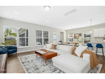 Bright living room featuring a white sectional sofa, wood floors, and natural light at 5009 Megara Run, Raleigh, NC 27603