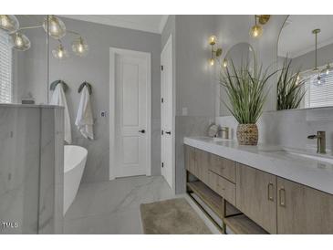 Stylish bathroom showcasing a luxurious soaking tub, double vanity with marble counters, and elegant lighting fixtures at 25 Westbourne Ln, Youngsville, NC 27596