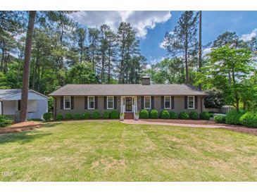 Charming single-story home with a manicured lawn, brick pathway, and lush green landscaping at 1305 Kimberly Dr, Raleigh, NC 27609