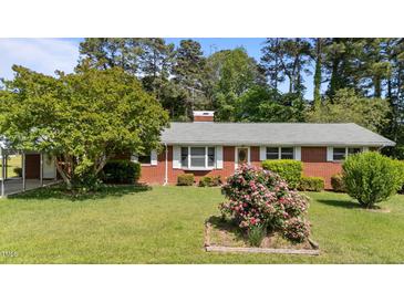 Charming brick home featuring a lush lawn and garden beds bursting with colorful flowers at 2910 Dove Ln, Raleigh, NC 27604