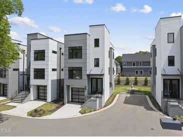 Modern townhome with gray and white facade, glass garage door, manicured lawn and blue sky at 221 Woodsborough Pl, Raleigh, NC 27601
