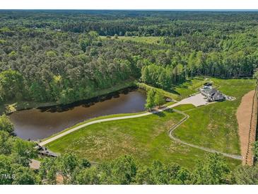 Stunning aerial view of the property featuring a lake, lush greenery, and a beautiful modern home with a swimming pool at 4001 Campbell Rd, Raleigh, NC 27606