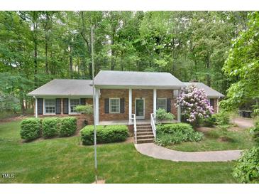 Charming brick home featuring a well-maintained lawn, mature trees, and a welcoming front porch at 5825 Scalybark Rd, Durham, NC 27712
