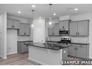 Modern kitchen with gray cabinets, black countertops, stainless steel appliances, and pendant lighting at 3918 Well Fleet Dr, Fuquay Varina, NC 27526