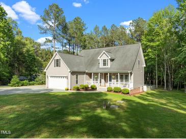 Charming home with a two-car garage, front porch, manicured lawn, and mature trees on a sunny day at 128 Madison Ct, Siler City, NC 27344
