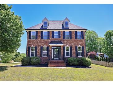 Charming two-story red brick home featuring black shutters, dormer windows, and well-maintained landscaping at 1009 Sarazen Dr, Clayton, NC 27527