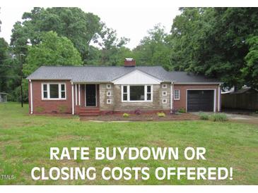 Charming brick home featuring a well-manicured front yard, a black roof, and an attached garage at 1610 W B St, Butner, NC 27509