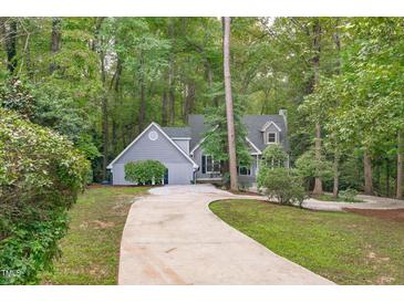 Charming gray home with a concrete driveway nestled in a lush, wooded landscape at 7116 Asheway Dr, Holly Springs, NC 27540