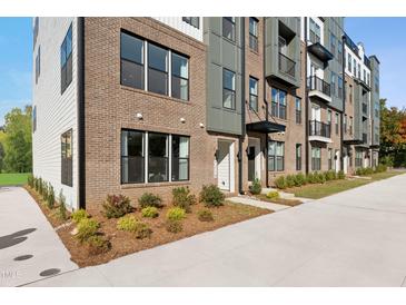 Modern townhome exterior featuring brick facade, black-framed windows, and landscaped front yard at 1242 Coach Station Aly # 101, Raleigh, NC 27601