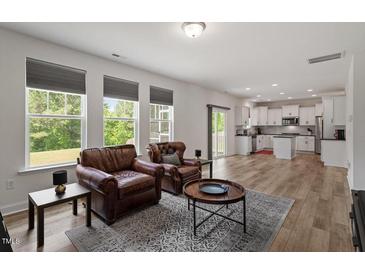 Bright living room featuring wood floors, large windows, and comfortable leather armchairs at 170 Creekhaven Dr, Angier, NC 27501