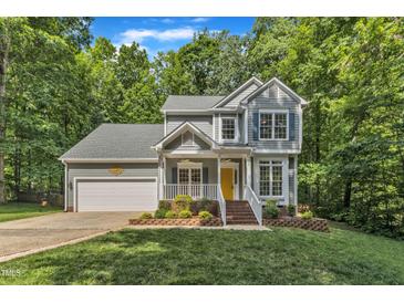 Charming two-story home with a yellow front door, lush landscaping, and a two car garage nestled amongst mature trees at 2513 Myrtle Ln, Hillsborough, NC 27278