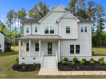 Charming two-story white home featuring a welcoming front porch, manicured lawn, and gray metal roof at 386 The Parks Dr, Pittsboro, NC 27312